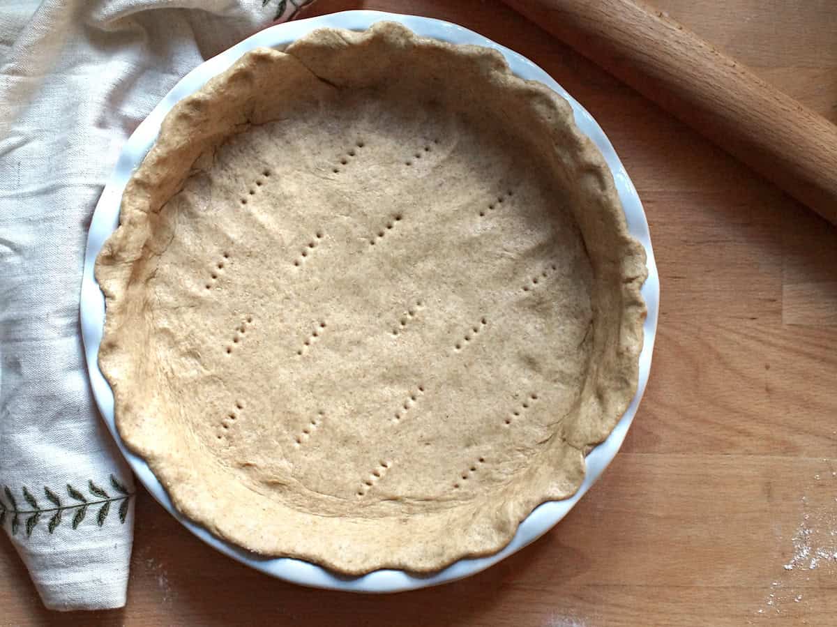 A deep dish pie pan is lined with the bready, yeasted dough for German Zwiebelkuchen. The bottom crust has been poked several times with a fork.
