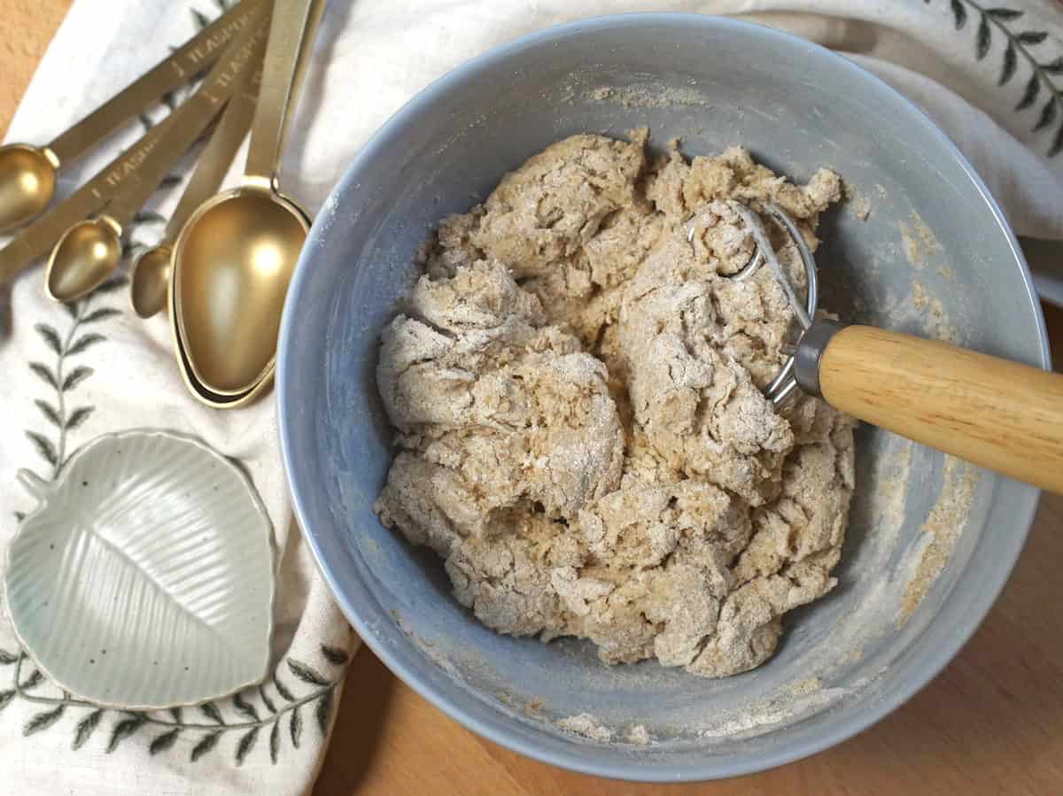A shaggy dough is being mixed with a danish dough hook in a pale blue ceramic bowl.