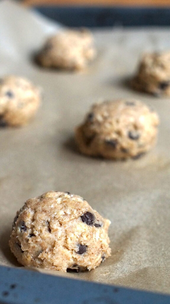 Spelt sourdough chocolate chip cookie dough rolled into balls, sitting on a lined baking tray.
