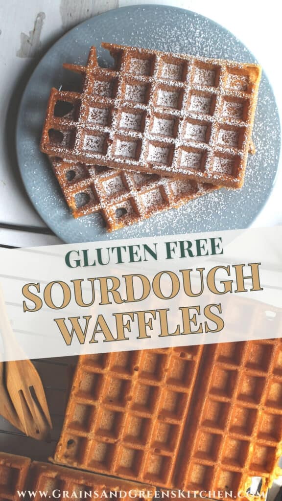 Two crispy, golden sourdough discard waffles, stacked on a pale blue plate, generously dusted with powdered sugar. The plate sits on a chipped white wooden surface, next to a cooling rack holding even more crispy waffles and a set of wooden knife and fork.