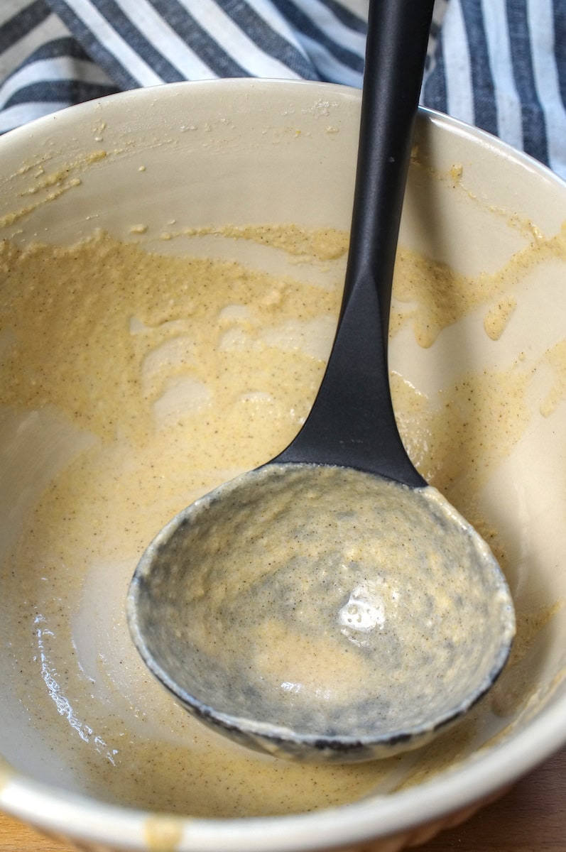 Emptied bowl of gluten free sourdough waffle batter. Traces of the batter coat the bowl and black ladle.