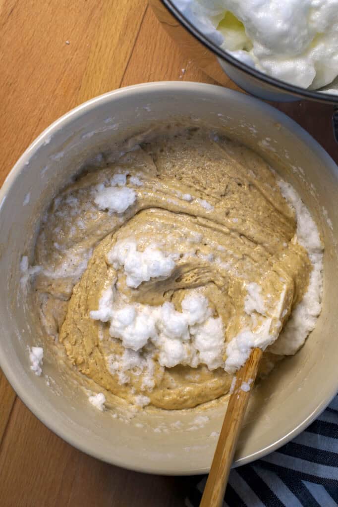 White, foamy flecks of egg whites, being folded into a thick yellow gluten free sourdough waffle batter.