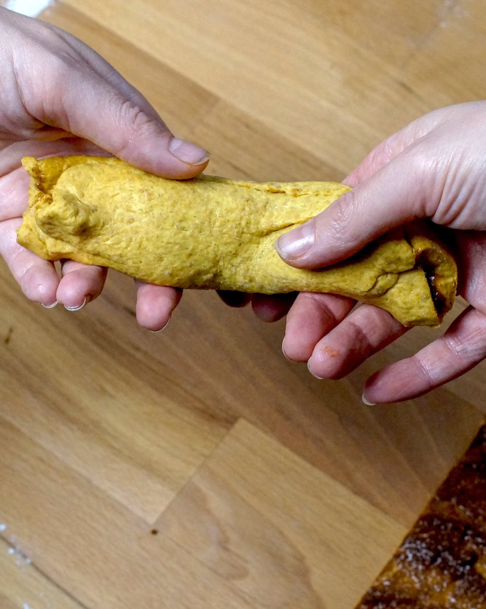 Two hands gently pressing a rolled up piece of cinnamon-swirled pumpkin sourdough bagel dough out into a rope.