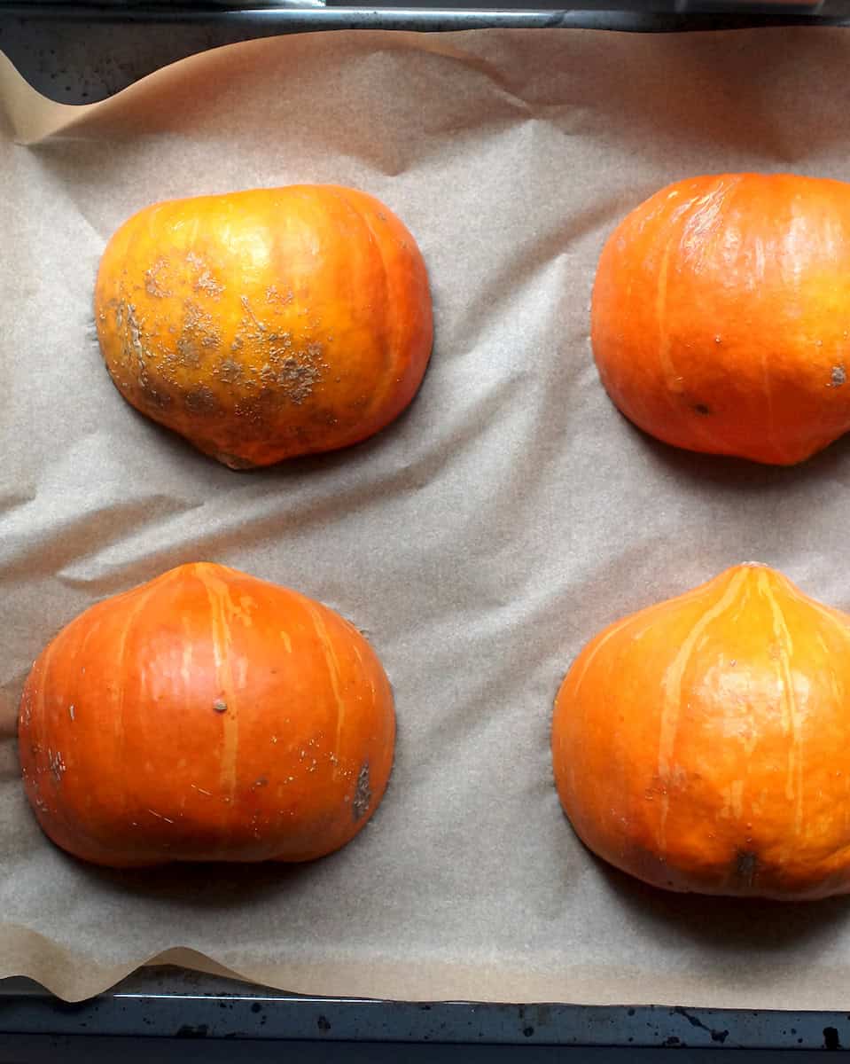 Four small pumpkin halves, sitting cut side down on a parchment-lined baking tray, roasted and ready for pureeing.