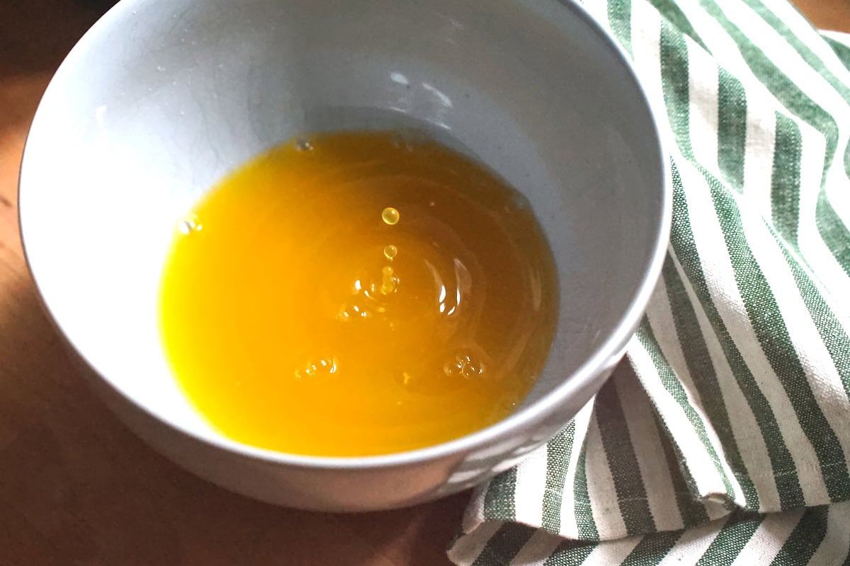 Pumpkin puree liquid being strained into a pale blue bowl, showing mid-air droplets and ripples from dripping puree.