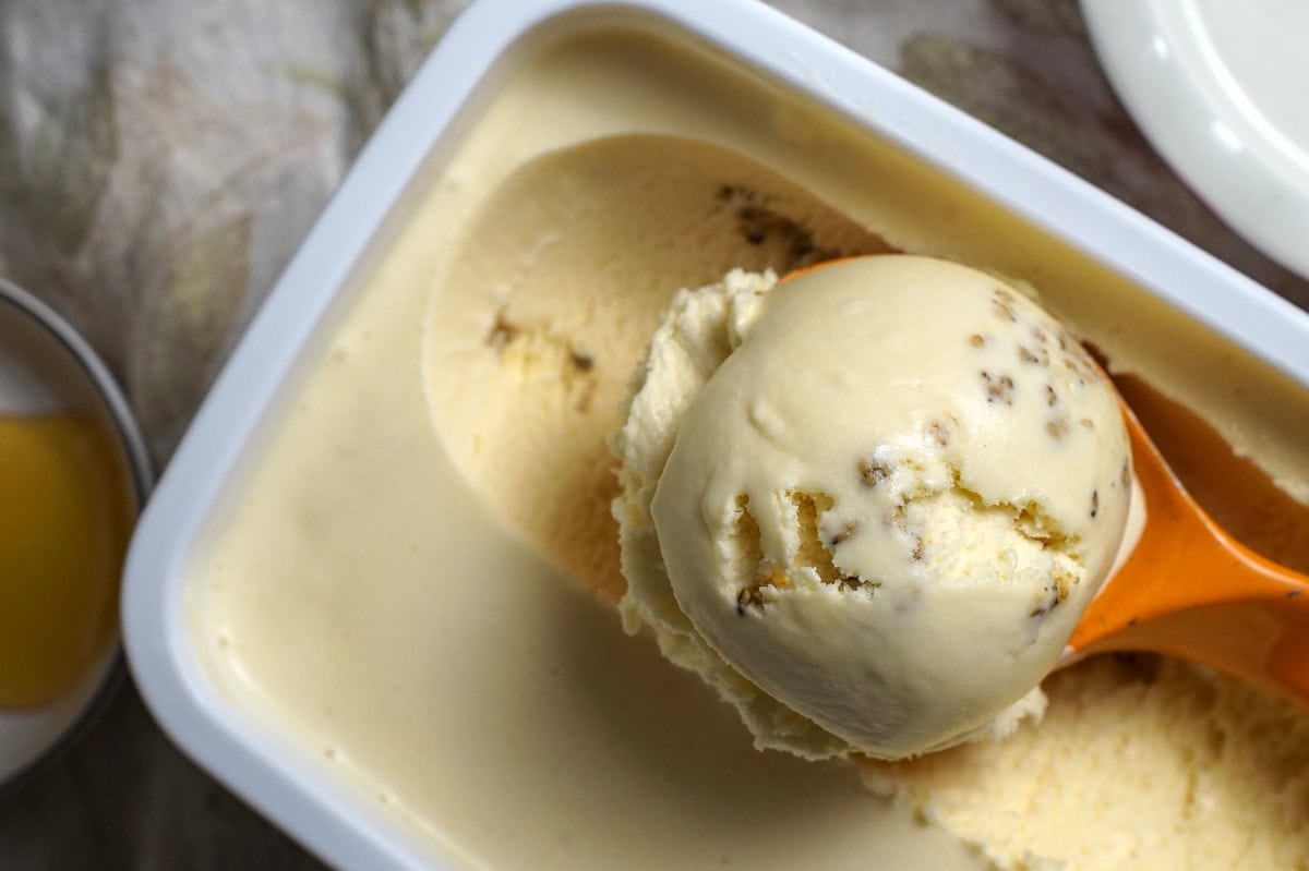 Close-up of a scoop of salted honey and sesame crunch ice cream in a orange spoon, resting on the surface of the ice cream container.