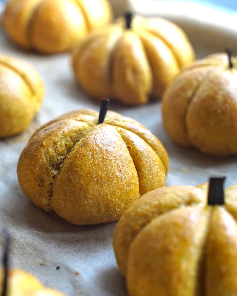 Baked and golden orange whole grain sourdough brioche buns, shaped as mini pumpkins on a lined baking sheet.