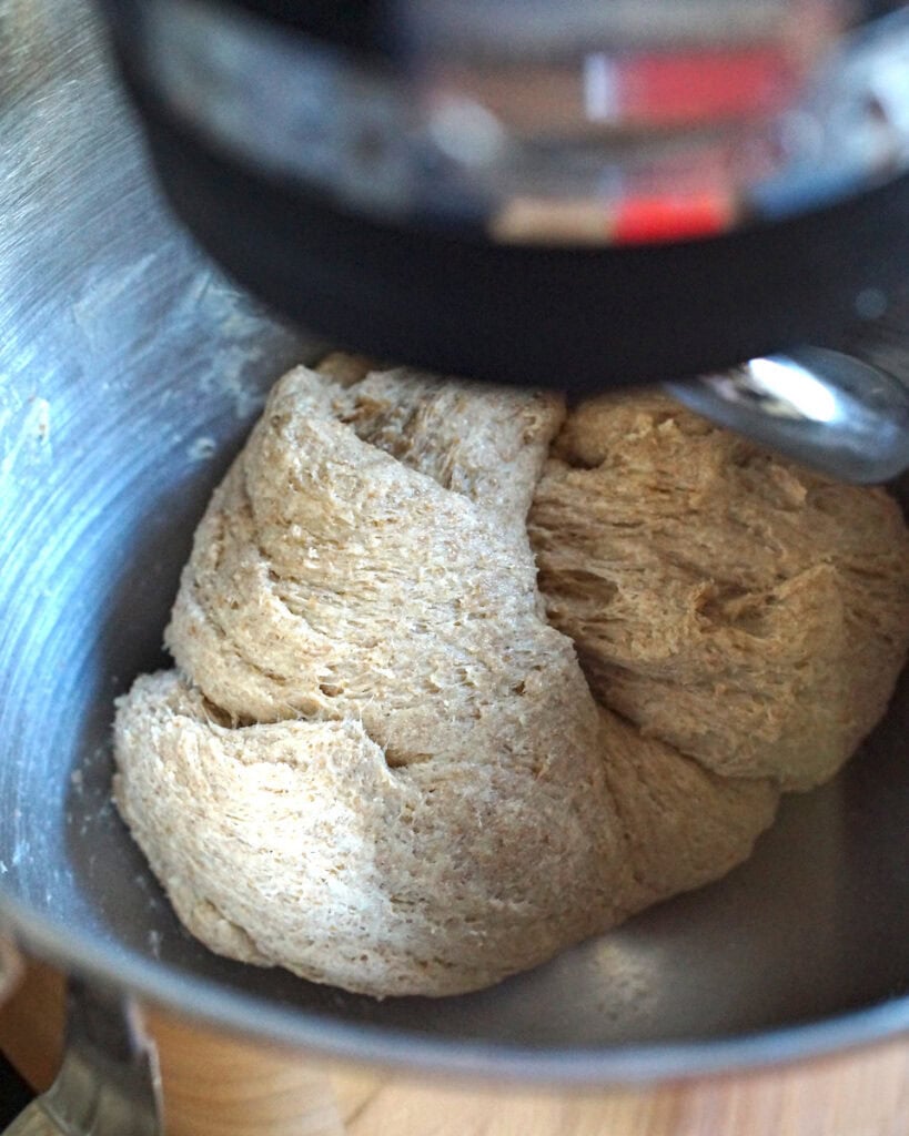 Whole wheat Swedish cinnamon roll dough being kneaded in a stand mixer, turning smooth.
