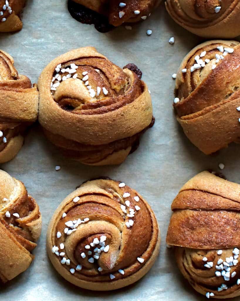 Large, fluffy whole wheat Swedish cinnamon rolls topped with pearl sugar, sitting on a lined baking sheet.