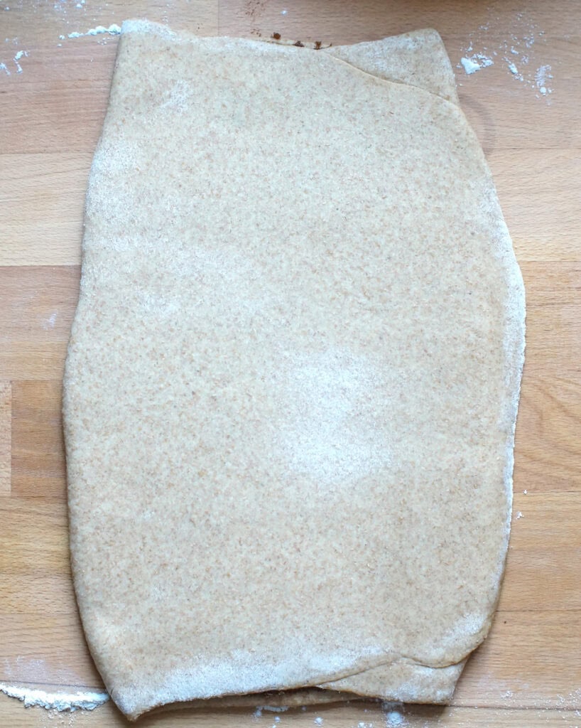 Filled and folded whole wheat cinnamon roll dough on a wooden work top.