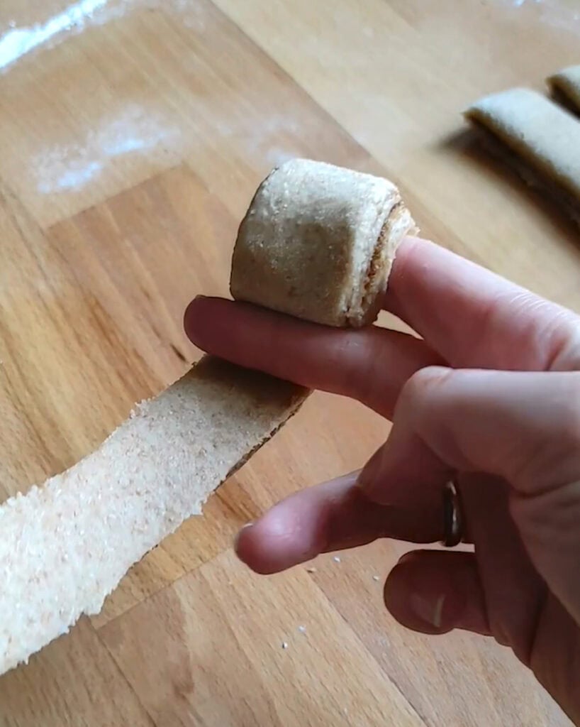 A filled strip of cinnamon roll dough wrapped around the index and middle finger, shaping a bun.