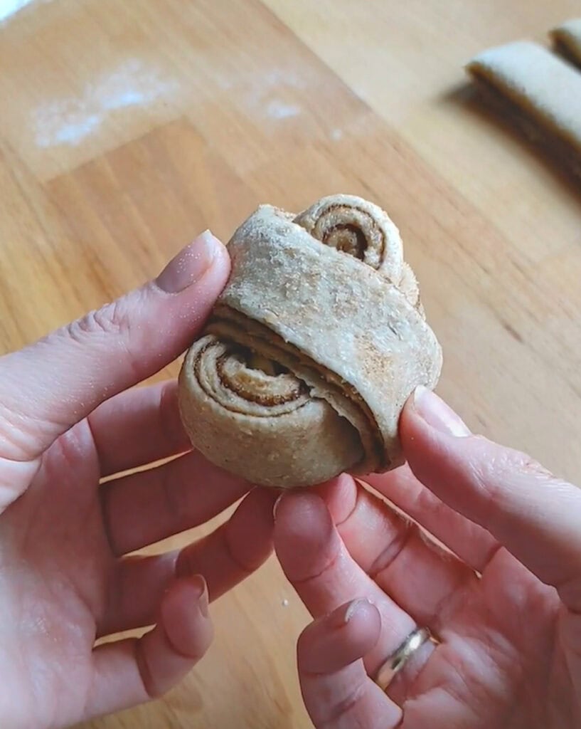 Two hands holding a shaped cinnamon bun, ready to go on the baking sheet.