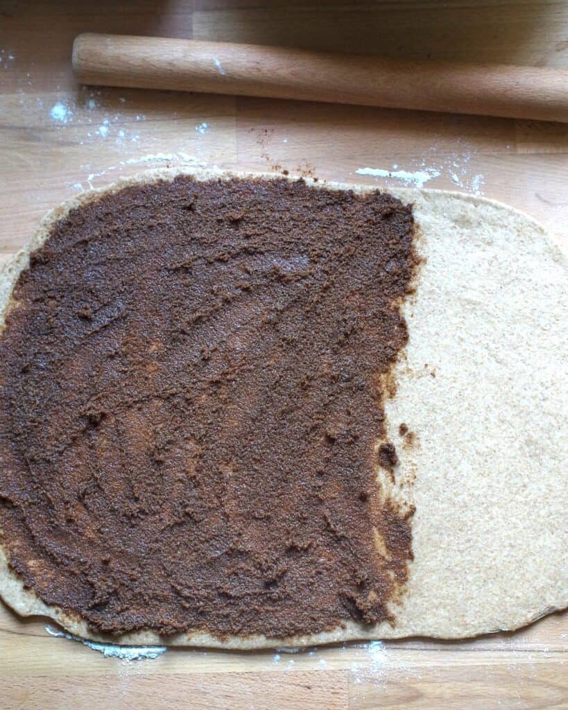 Rolled out whole wheat cinnamon roll dough rolled out and two-thirds spread with cinnamon sugar filling.