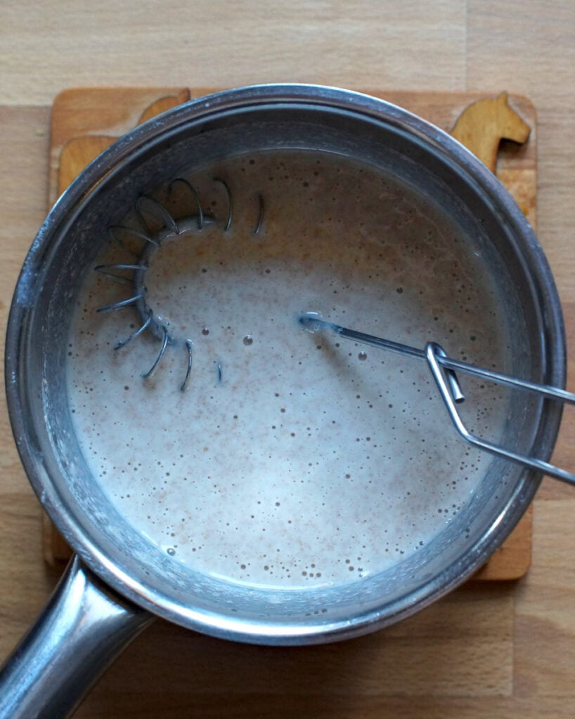 Tangzhong roux with added milk in a small stainless steel pot on a wooden coaster.