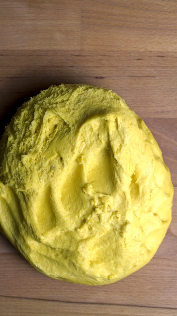 A soft, golden dough is turned out upside down onto an unfloured wooden kitchen counter.