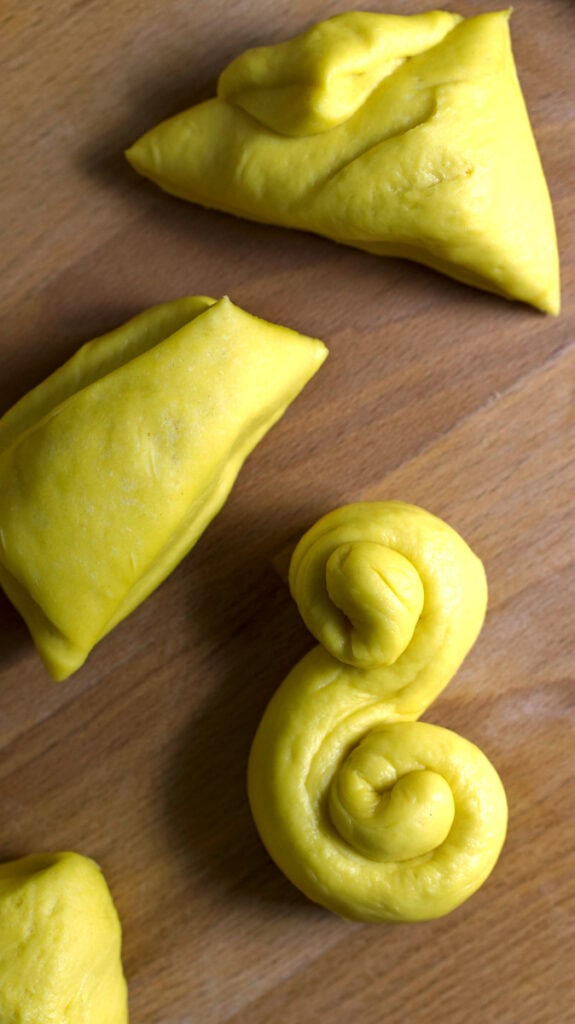 Portioned out pieces of sourdough saffron bun dough, next to an S-shaped lussekatter bun.