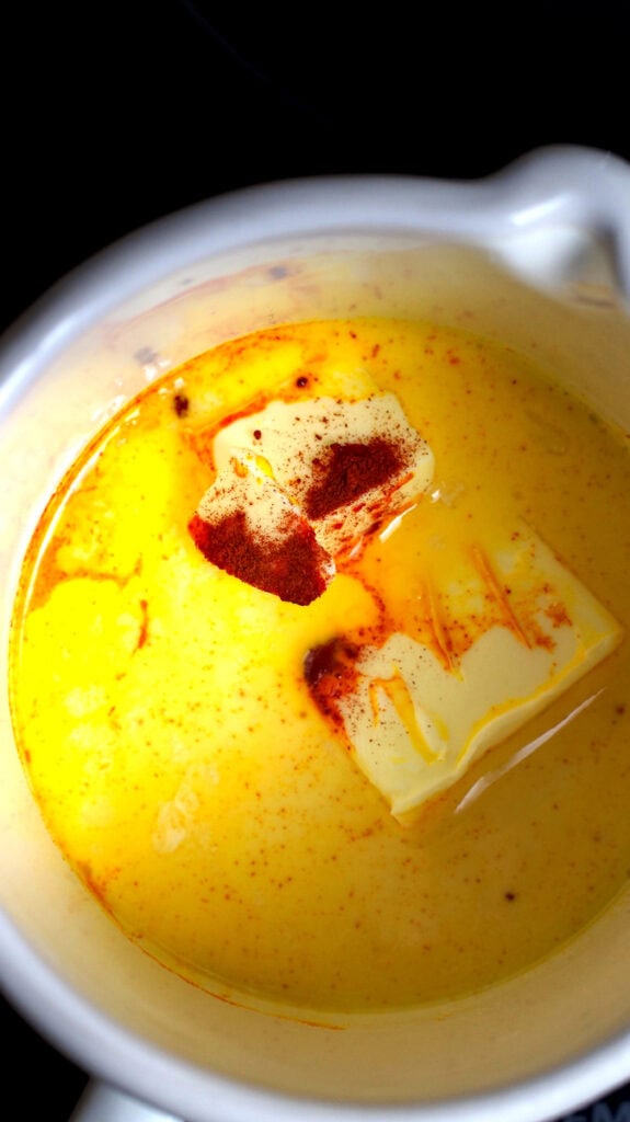 Vibrant orange colored saffron-milk and butter being warmed in a pot.