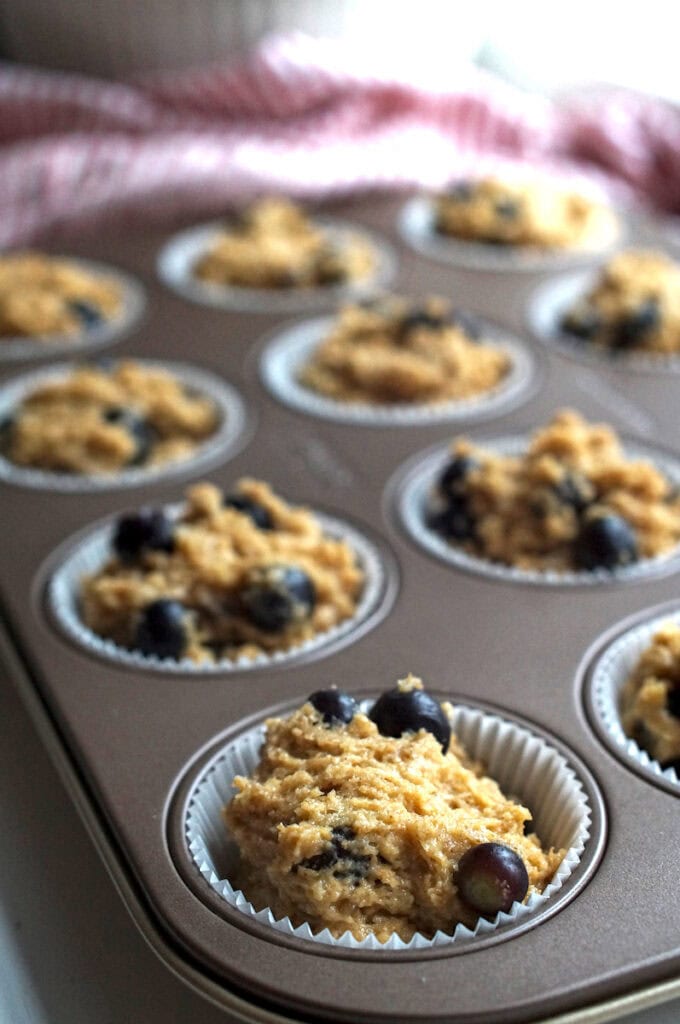 Close-up of muffin tin with thick batter portions, each loaded with juicy blueberries, prepped for baking into sourdough blueberry muffins.