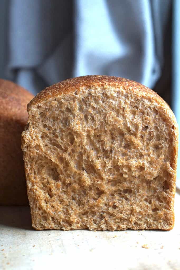 Close-up of a brioche-style sourdough sandwich bread loaf made with fresh milled soft wheat flour, split to show fluffy, brioche-like crumb on a wooden cutting board.