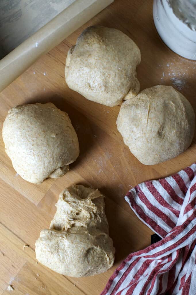 Four pre-shaped balls of European-style whole wheat sourdough sandwich bread dough made with fresh milled flour on a worktop.
