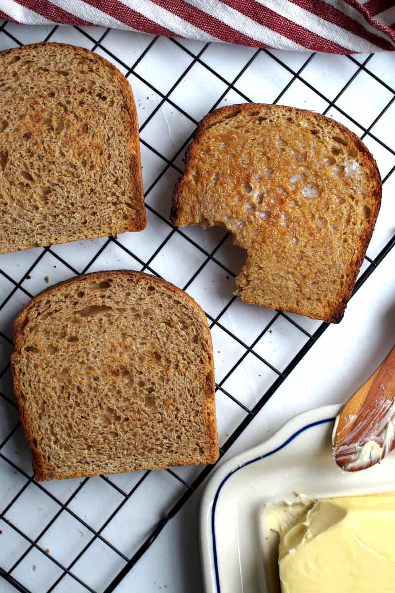 Three toasted slices of brioche-style whole wheat sourdough sandwich bread with fresh milled flour, one buttered with a bite.