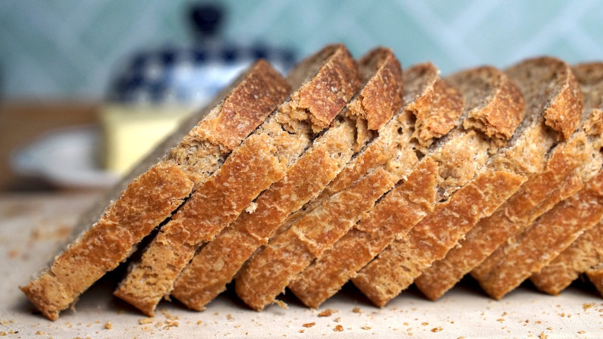 Side close-up of European-style sourdough sandwich bread slices made with fresh milled whole wheat flour, leaning in a row with a butter dish in the background.