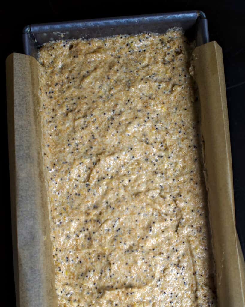 Mixed lemon poppy seed batter in a parchment-lined loaf pan, ready for baking